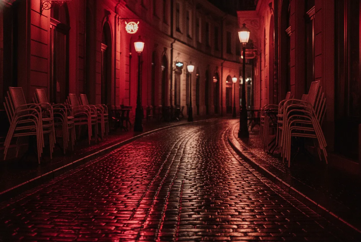 La vieille ville de Bucarest après la pluie : pavés mouillés qui reflètent les lumières des bars, chaises vides.