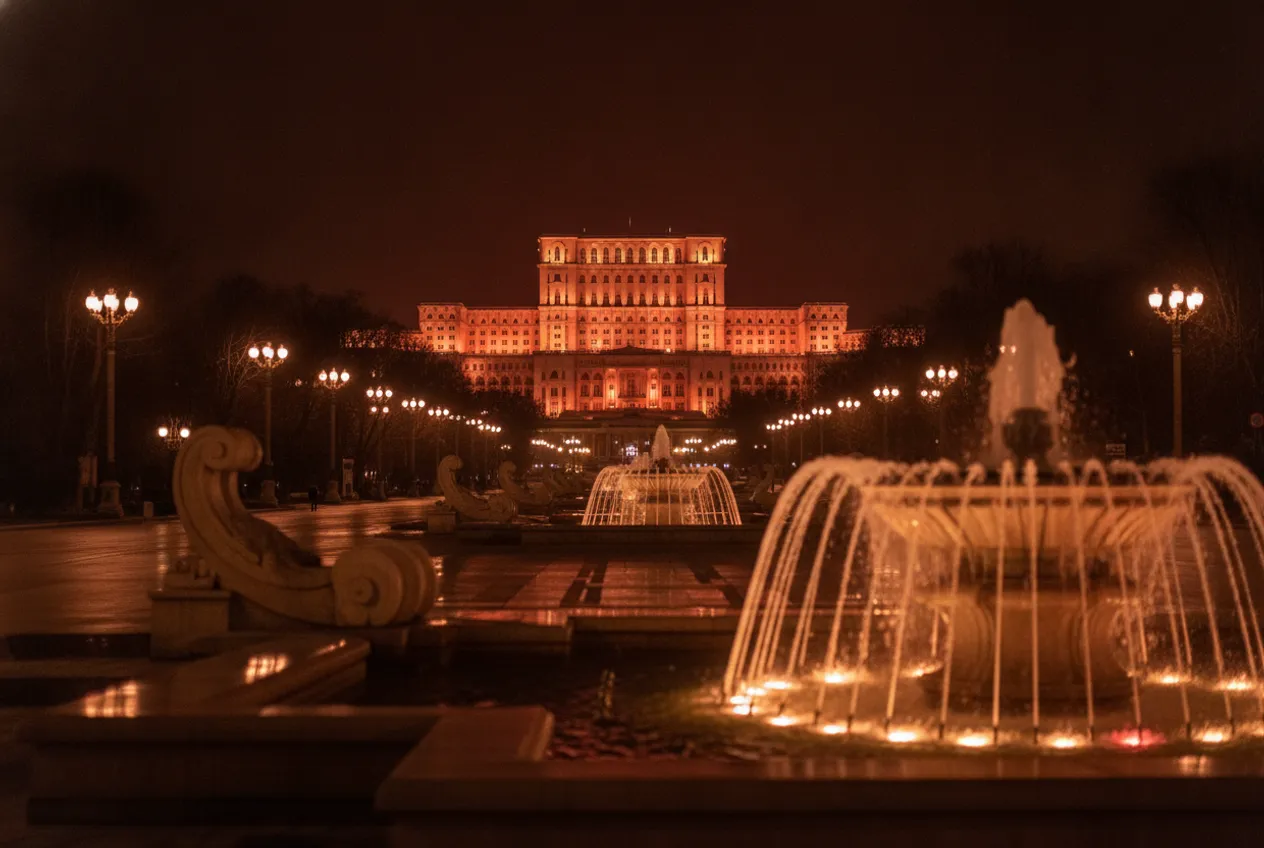La place Unirii la nuit : fontaines illuminées et, au bout du boulevard, le Palais du Parlement.
